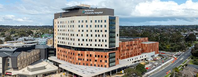 Aerial view of a hospital, a large multi-story building in an urban setting, with visible landscaping and adjacent structures.