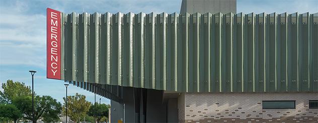 Exterior view of a modern hospital emergency department with a red emergency sign on the side.