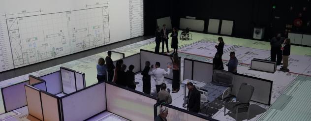 People standing on and around a large-scale hospital floor plan projection, reviewing room layouts and clinical spaces in an immersive design environment.