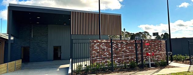 Modern building behind a black fence with a decorative brick wall and landscaped garden.